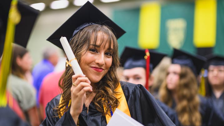 This is a photograph of a female student holding up her diploma during the 2024 commencement ceremony.