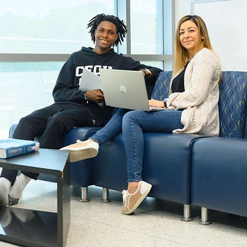 Three Cecil College students in the Engineering and Math lounge sitting at desks and talking with books