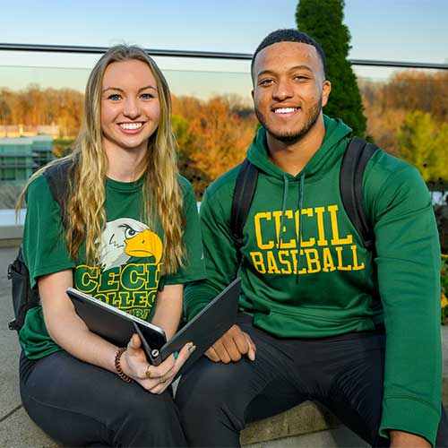 A female and a male Cecil College student sitting outside on campus holding books.