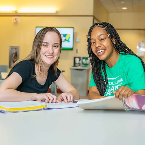 Two female students sitting in the student lounge at Cecil College, holding books and smiling.