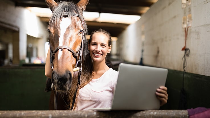 Cecil College Equine Studie Certificates - Woman in a stable with a horse and a laptop.