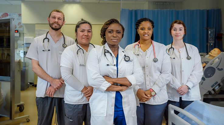 Cecil College Nursing Degrees & Certificates - Nursing students standing in a mock-up healthcare facility/classroom.